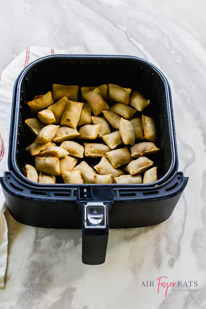 Vertical picture showing cooked pizza rolls in the air fryer basket. The basket is black. The pizza rolls are a golden brown.