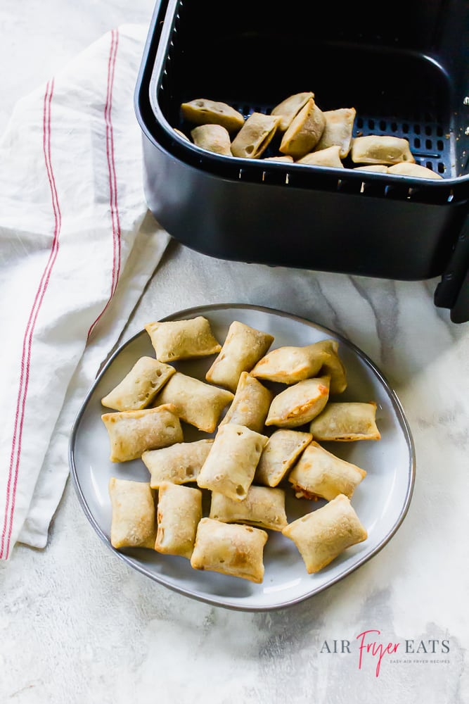 cooked pizza rolls on a white plate on the bottom of the vertical picture. Pizza rolls in a black air fryer basket on the top of the picture.