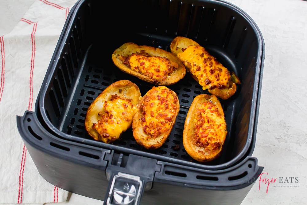 loaded potato skins in black air fryer basket with a white and red napkin to the left side.