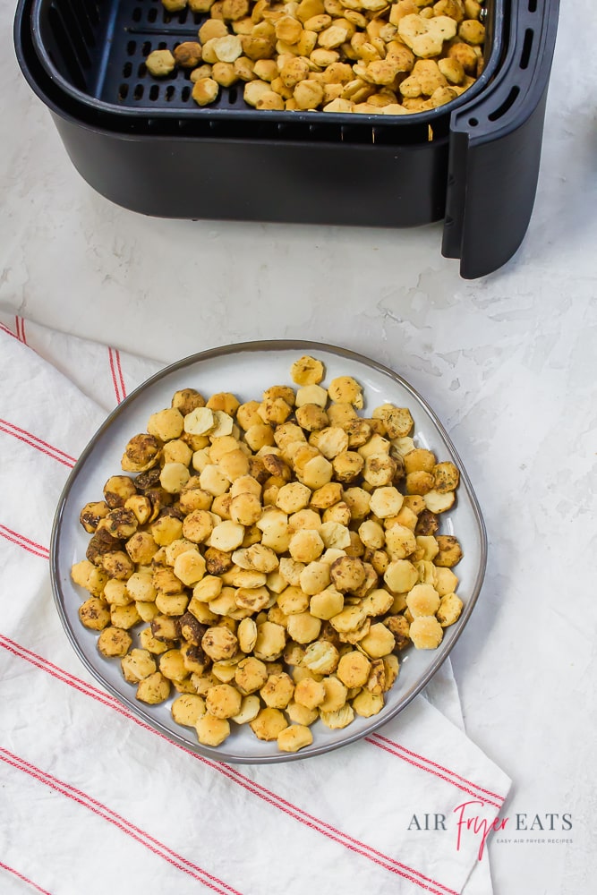 Vertical photo showing oyster crackers in a black air fryer basket at the top and oyster crackers on a white plate at the bottom of the photo.