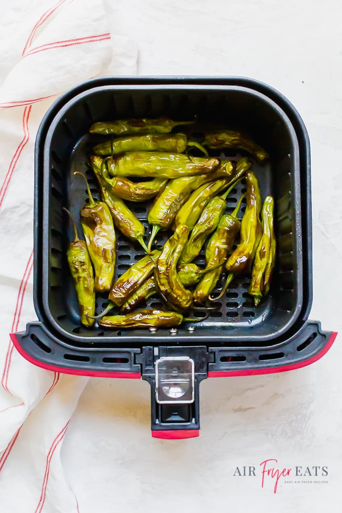 vertical overhead picture of blistered and cooked peppers in a red and black air fryer basket.