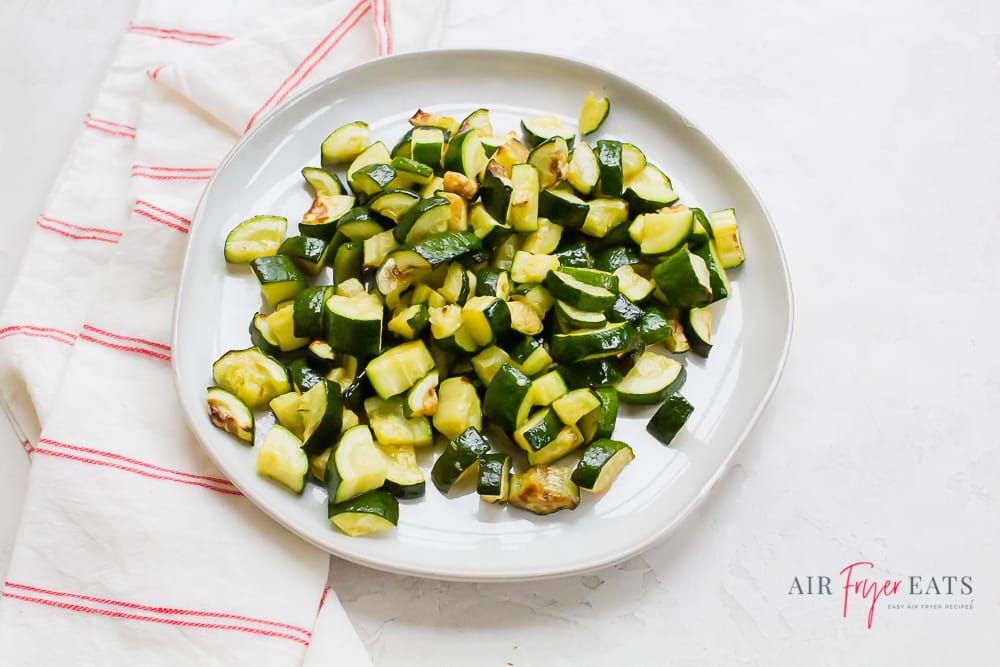 cooked zucchini on a white plate with a red plaid kitchen towel