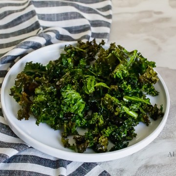 kale chips on a white plate with a blue striped kitchen towel on a marble countertop