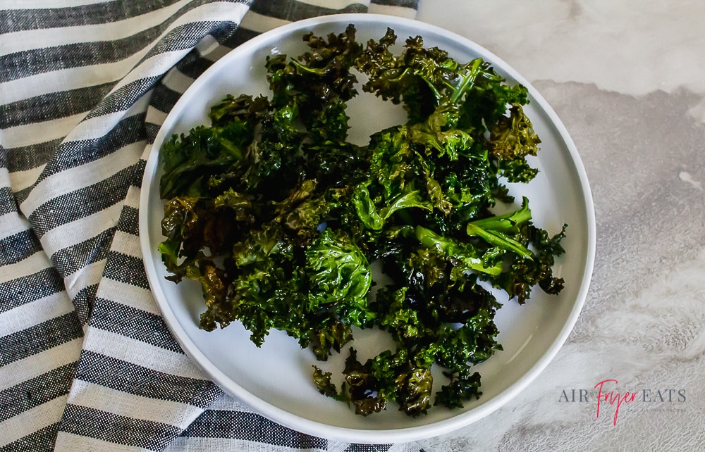 kale chips on a white plate with a gray striped kitchen towel on a marble countertop