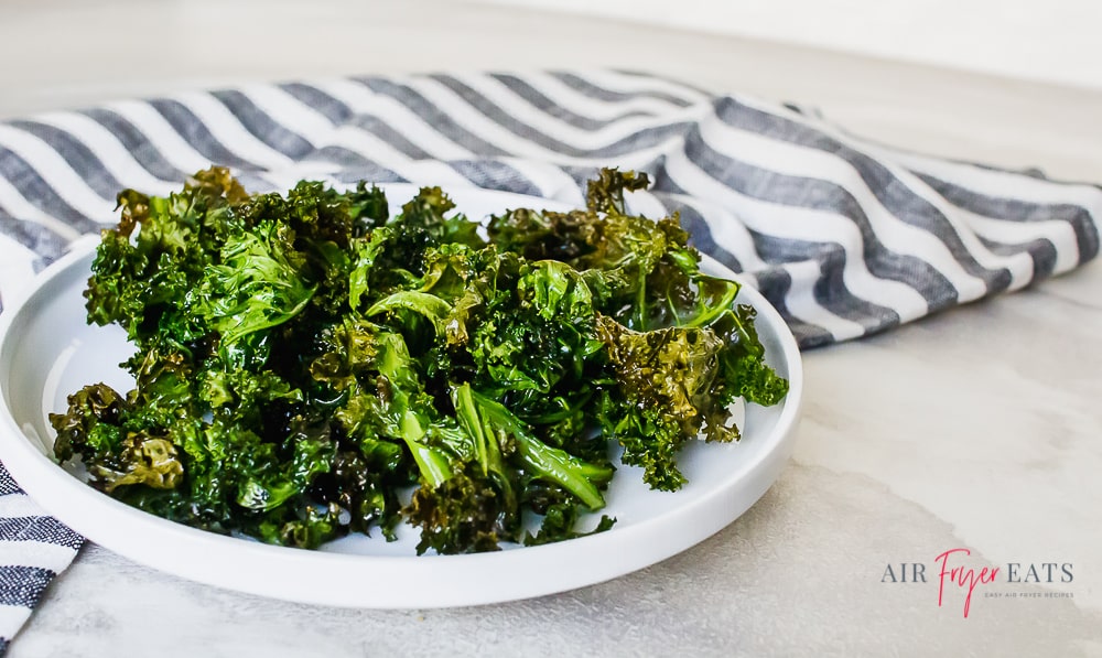 kale chips on a white plate with a gray striped kitchen towel