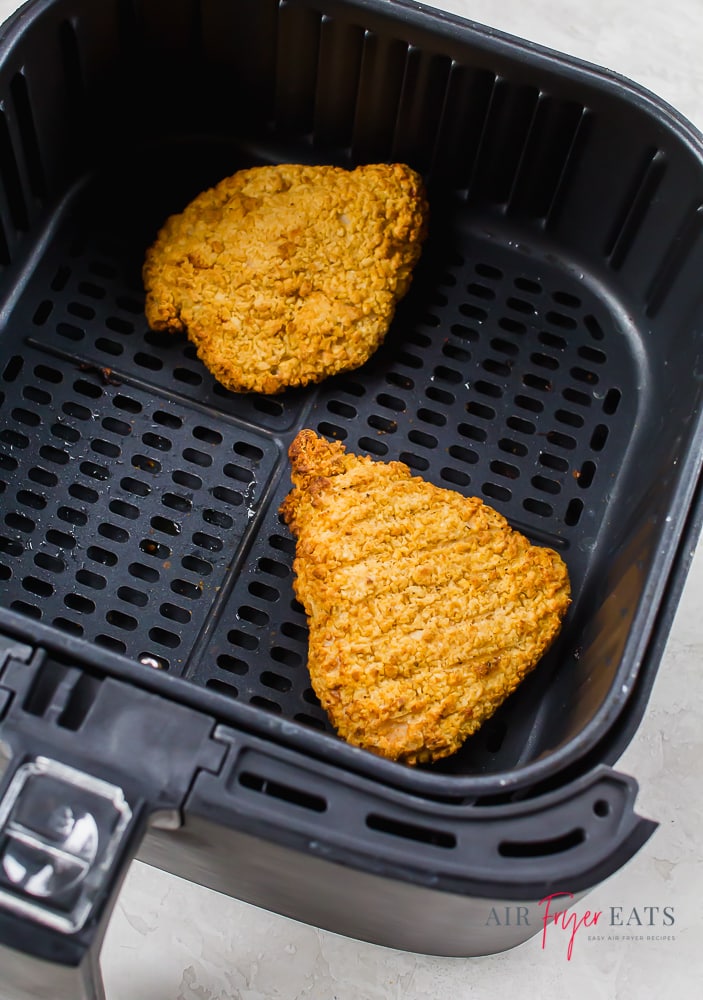 vertical picture of two breaded chicken breasts in a black air fryer basket