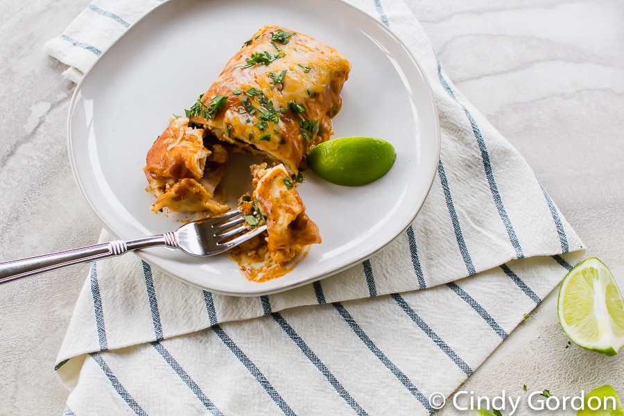 vegetarian enchiladas on a white plate with a fork and a lime wedge