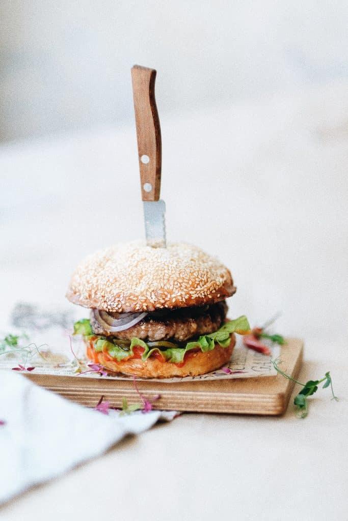 vertical photo of a hamburger and bun with a knife stuck in it
