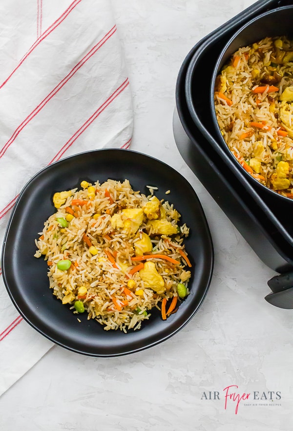 Fried rice on a black plate next to an air fryer basket of fried rice