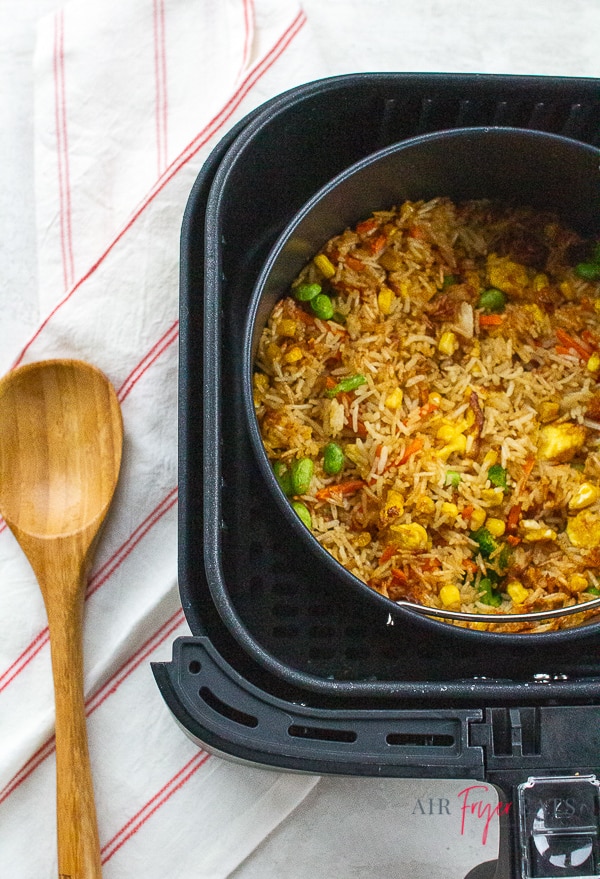 fried rice in an air fryer basket next to a wooden spoon and striped kitchen towel