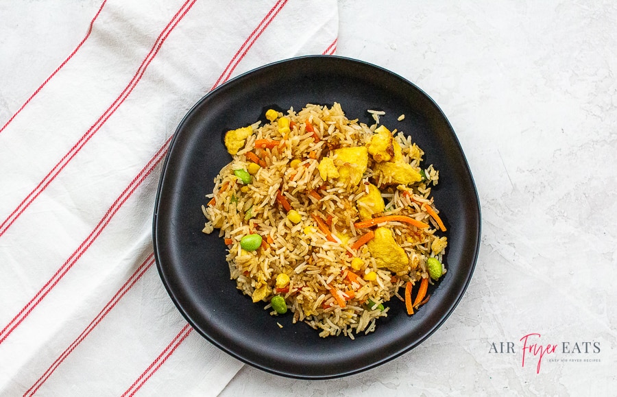 fried rice on a black plate on a marble countertop next to a red striped kitchen towel