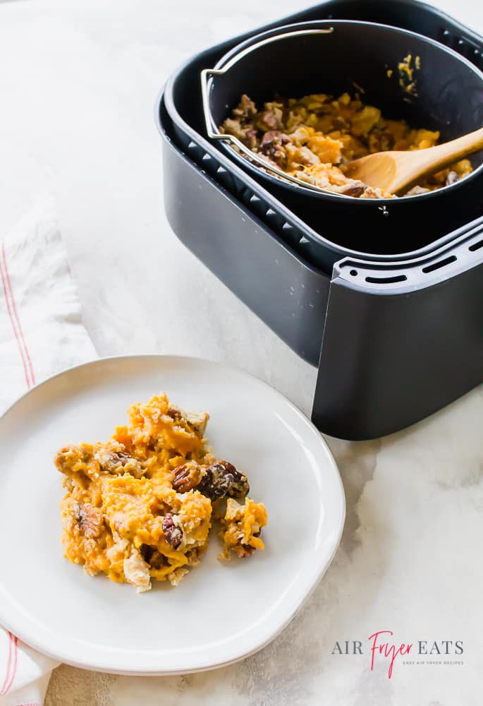 Picture of sweet potato casserole in a black air fryer basket with a wooden spoon and also on a white plate.