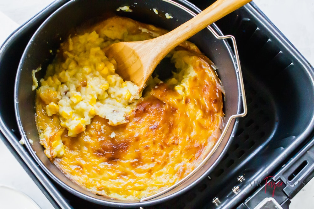 image of creamed corn casserole in a black air fryer basket with a wooden spoon