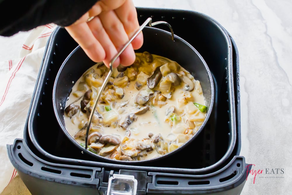 hand putting the air fryer green bean casserole into the black air fryer basket