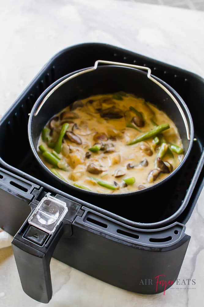 green bean casserole in a black oven safe pot inside of a black air fryer basket