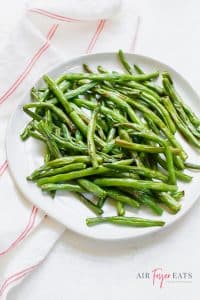 air fryer green beans on a white plate, with a white ad red napkin to the left