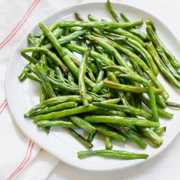 air fryer green beans on a white plate, with a white ad red napkin to the left