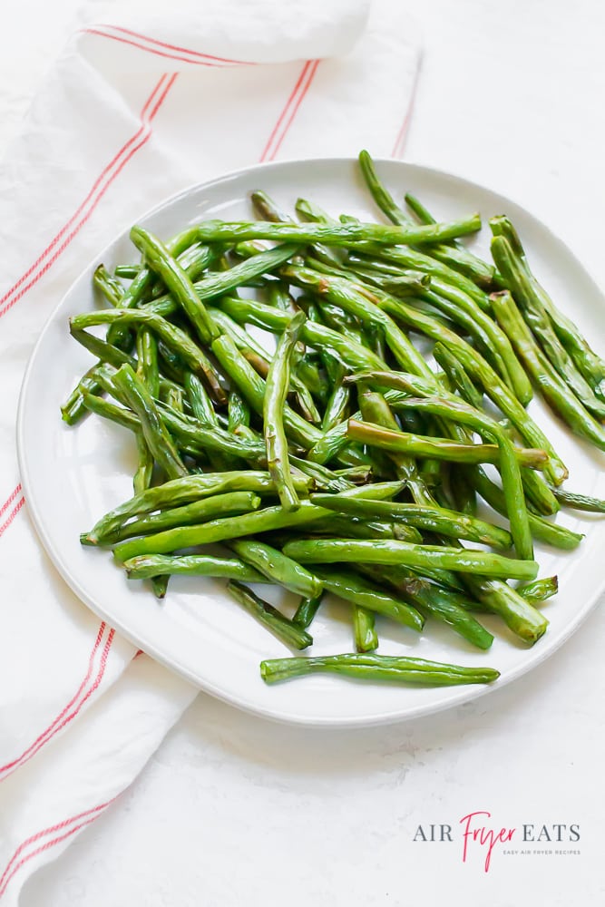 cooked green beans on a white plate next to a red striped kitchen towel