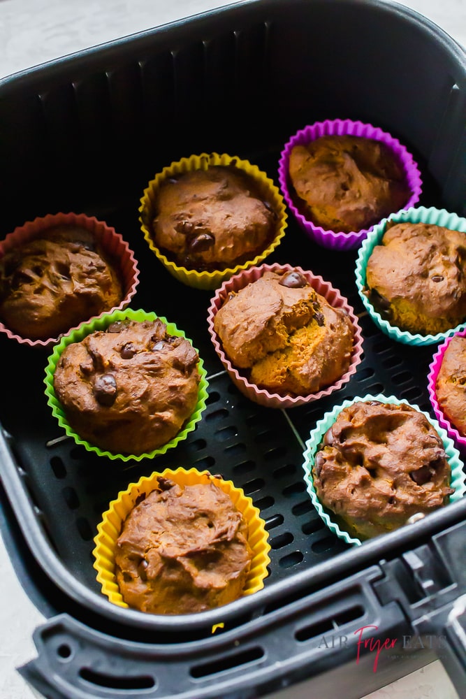 vertical picture of cooked muffins in colorful muffin cups inside of a black air fryer basket