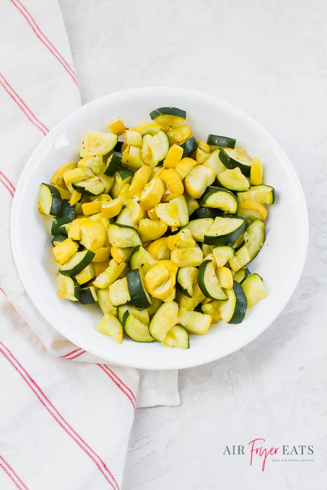cooked yellow squash and zucchini in a white bowl on a white background with a red/white napkin to the left