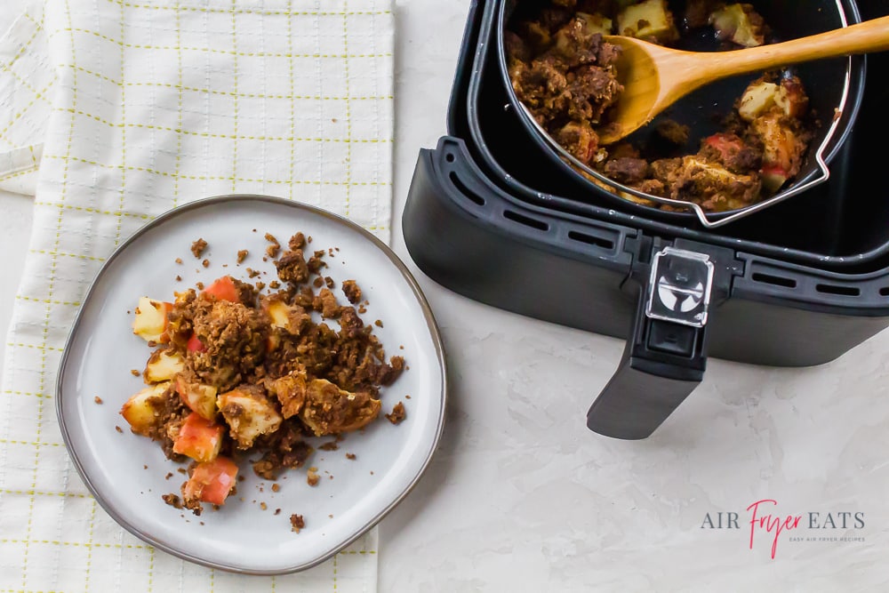 air fryer apple crisp on a white plate. Then more air fryer apple crisp in a black air fryer pot in a black air fryer basket.