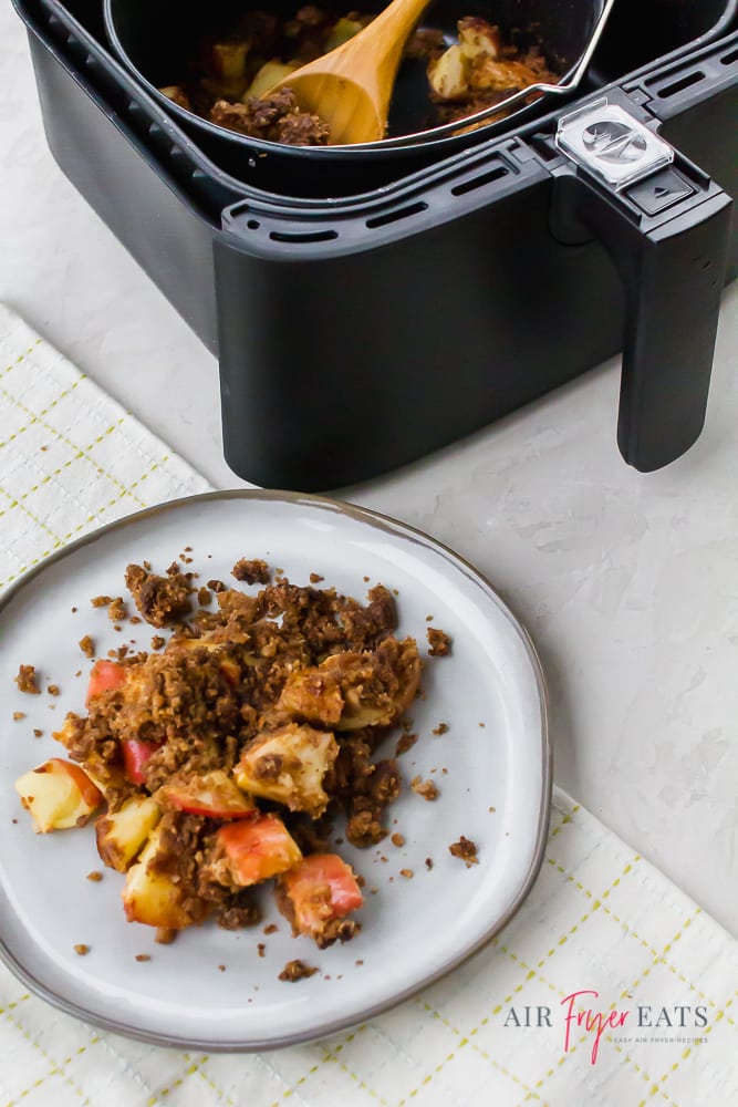 air fryer apple crisp served on a white plate. Also some in a black air fryer basket to the top of the vertical picture.