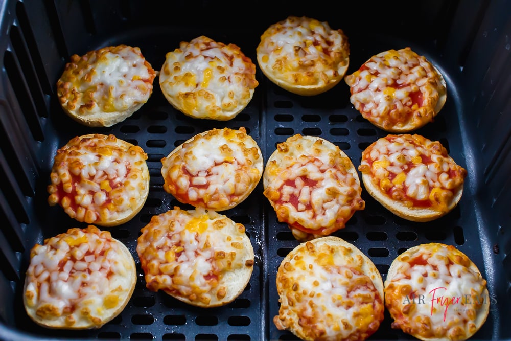 horizontal picture of a black air fryer basket with cooked cheese bagel bites inside.