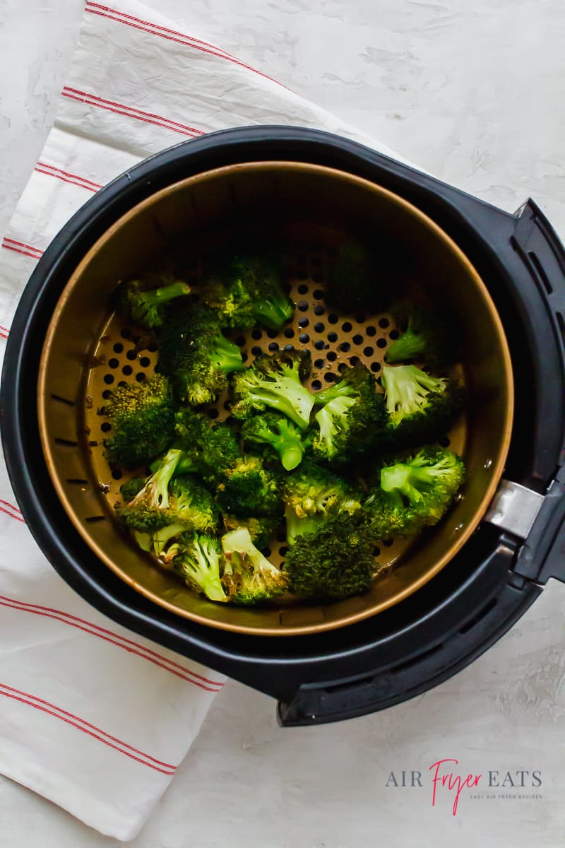 Cooked air fryer broccoli in a black and gold air fryer round basket
