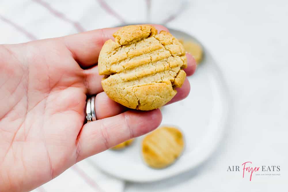 Someone holding a peanut butter cookie over a plate of cookies