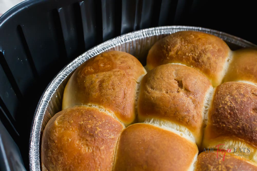 close up angle of cooked air fryer rolls in a pie tin in a black air fryer baskets