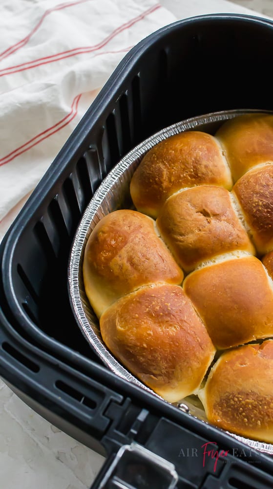 Side angle of frozen rolls cooked in an air fryer. Rolls  are in a foil pan in a black air fryer basket