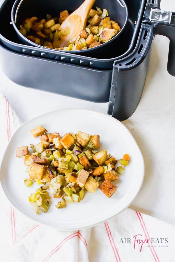 picture of air fryer stuffing in a black air fryer basket with a wooden spoon. air fryer dressing is also on a white plate.