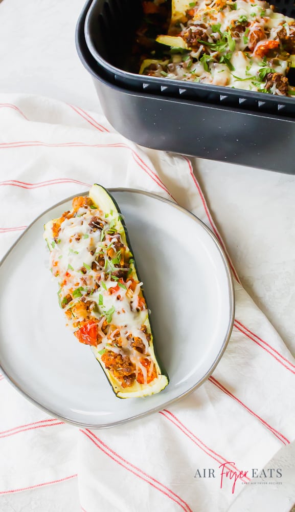 cooked zucchini stuffed with tomatoes, peppers, and cheese on a white plate