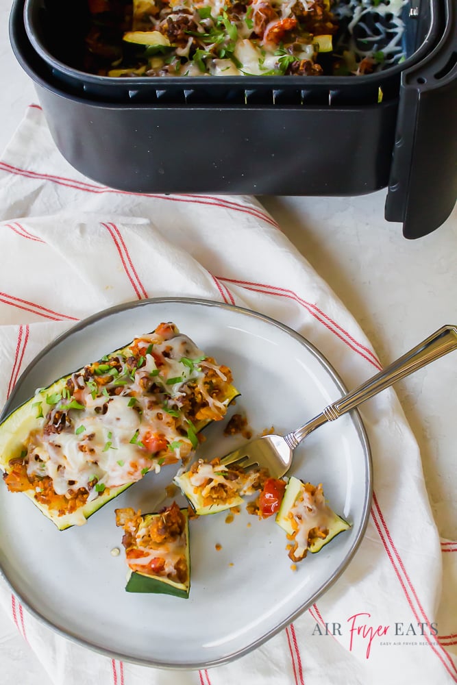 stuffed zucchini boat cut into pieces on a white plate next to an air fryer basket