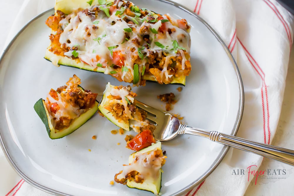 pieces of a stuffed zucchini boat on a white plate with a fork