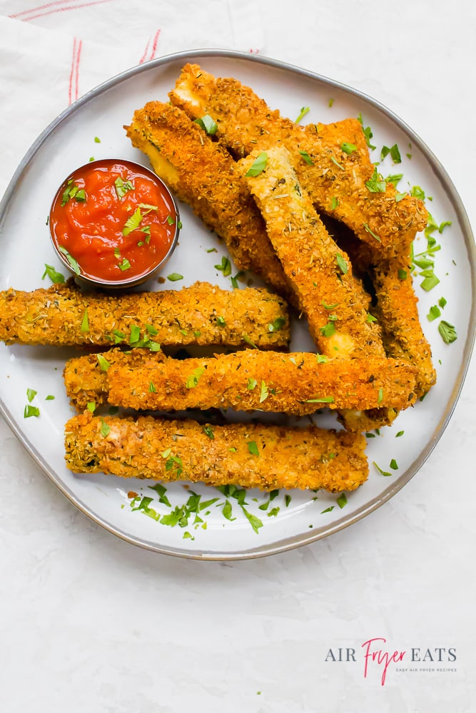 zucchini fries on a white plate garnished with parsley and served with marinara