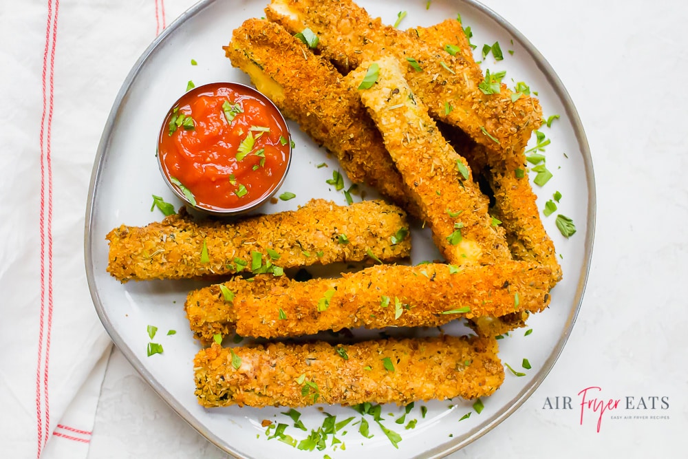 A white plate of zucchini fries garnished with parsley and a marinara dipping sauce