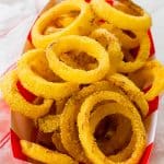Crispy onion rings in a cardboard tray on a red and white striped kitchen towel