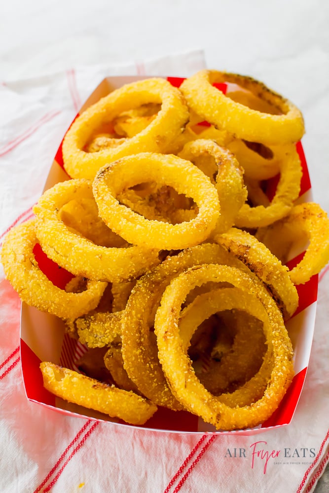 Crispy onion rings in a cardboard tray on a red and white striped kitchen towel