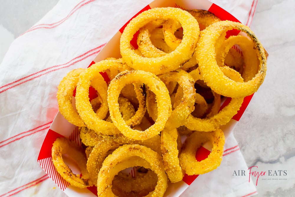 Overhead shot of cooked onion rings in a red and white striped cardboard container
