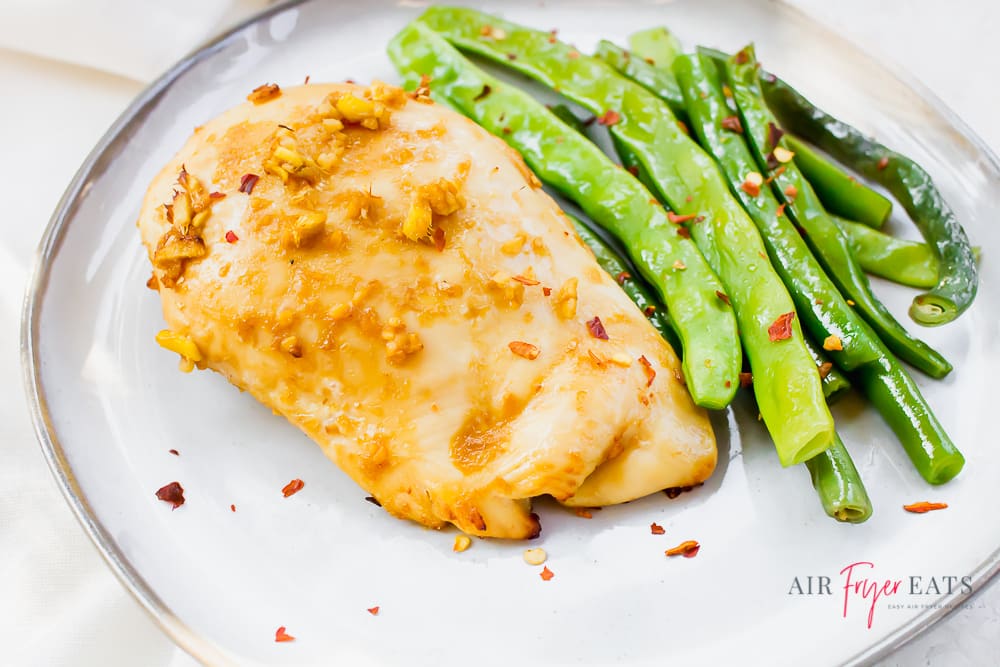 Ginger chicken and green beans garnished with crushed red pepper flakes on a white plate