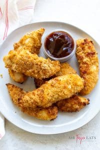 Vertical picture of cooked air fryer chicken tenders on a white plate