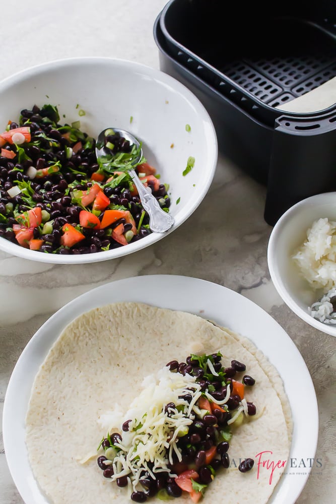 a bowl of beans and veggies, an air fryer, and a plate topped with an unrolled burrito