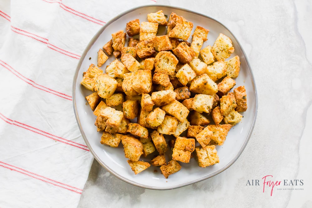 Homemade croutons on a white plate with a red striped kitchen towel
