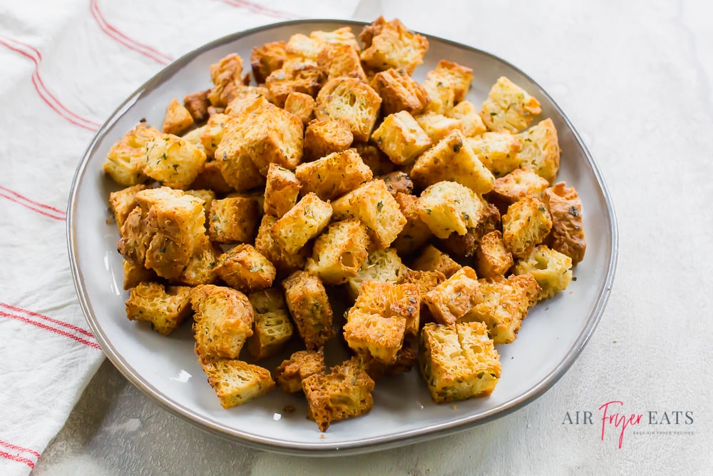 Homemade croutons on a white plate and granite countertop with a striped kitchen towel