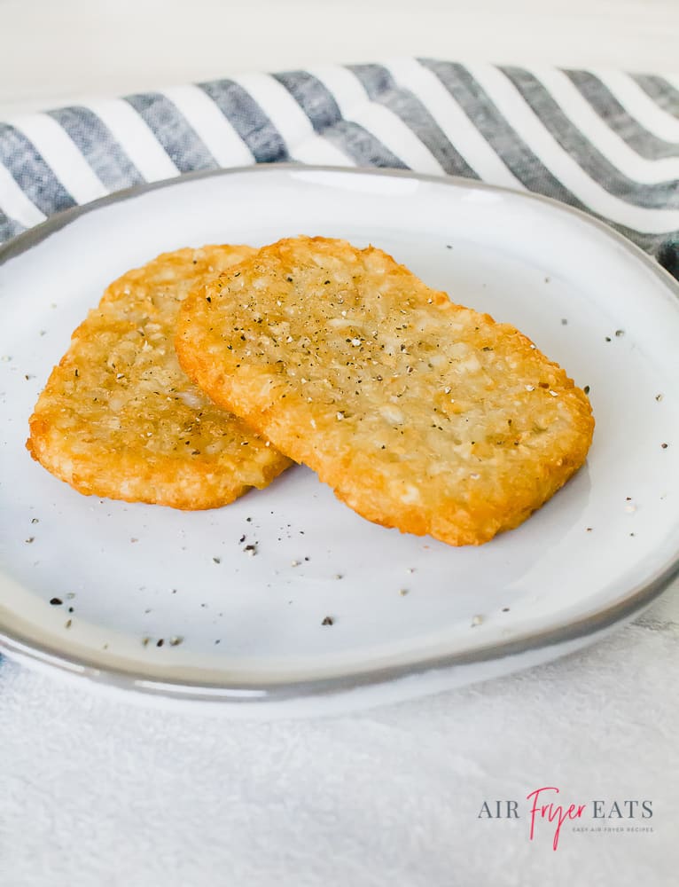 A pair of golden brown hash browns on a white plate with pepper