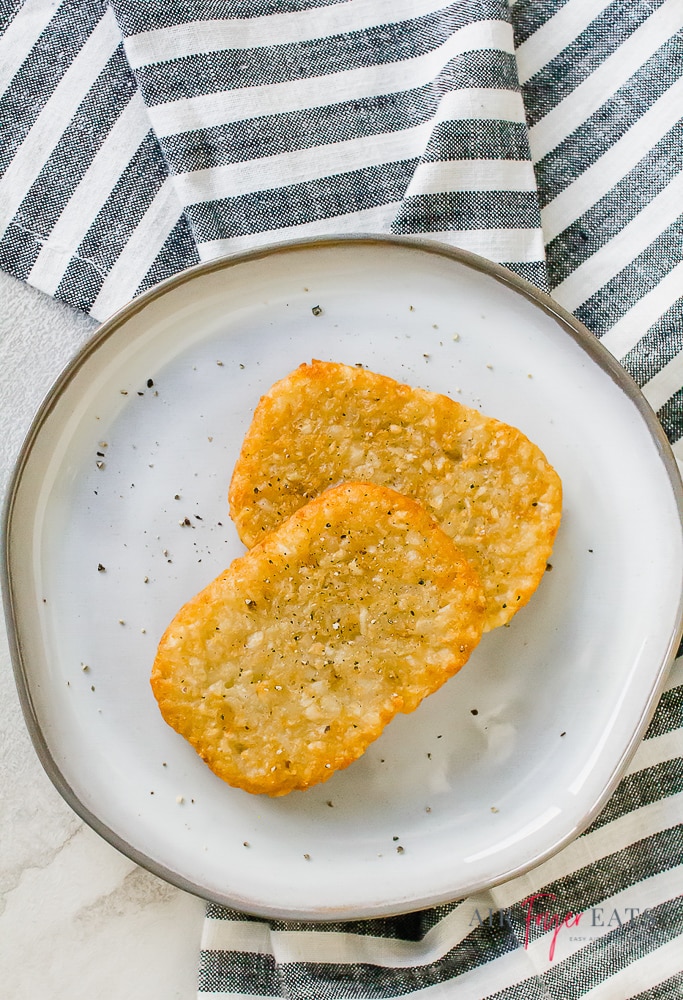 Two cooked hash browns sprinkled with pepper on a white plate