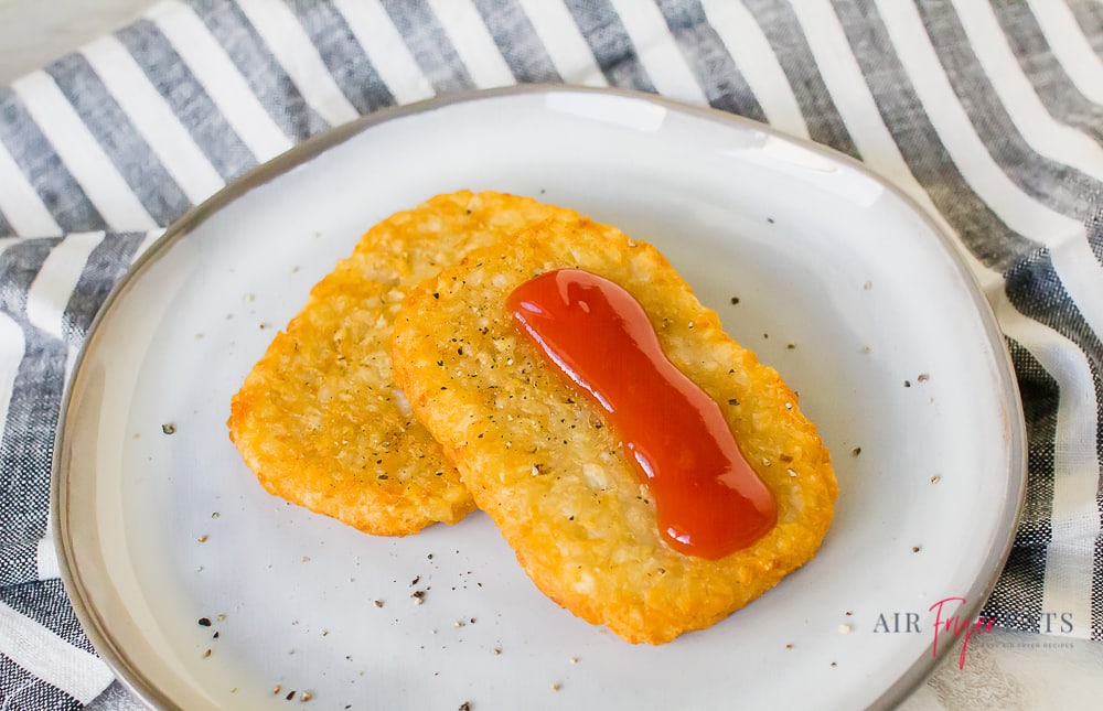 Two hash browns stacked together and garnished with ketchup and pepper on a white plate