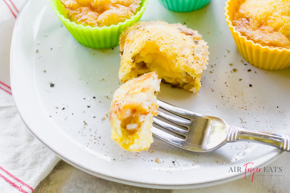 Scrambled egg cups on a white plate with one bite on a fork