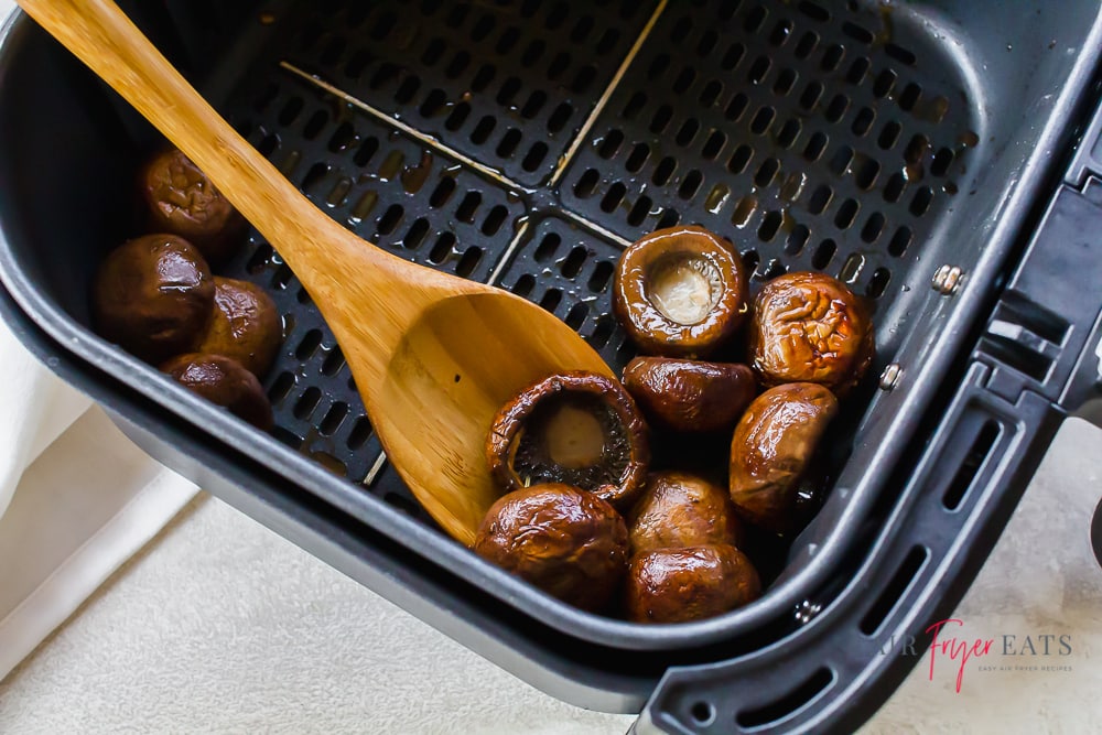Air fryer basket with mushrooms being spooned out